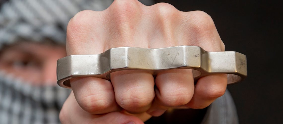 A man brandishes a set of brass knuckles toward camera